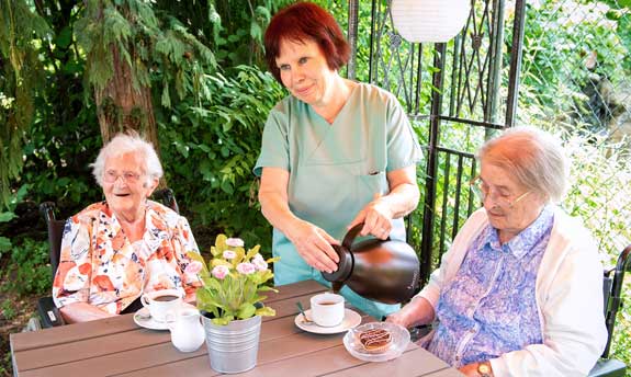 Pflegerin mit Bewohnern beim Kaffee im Garten